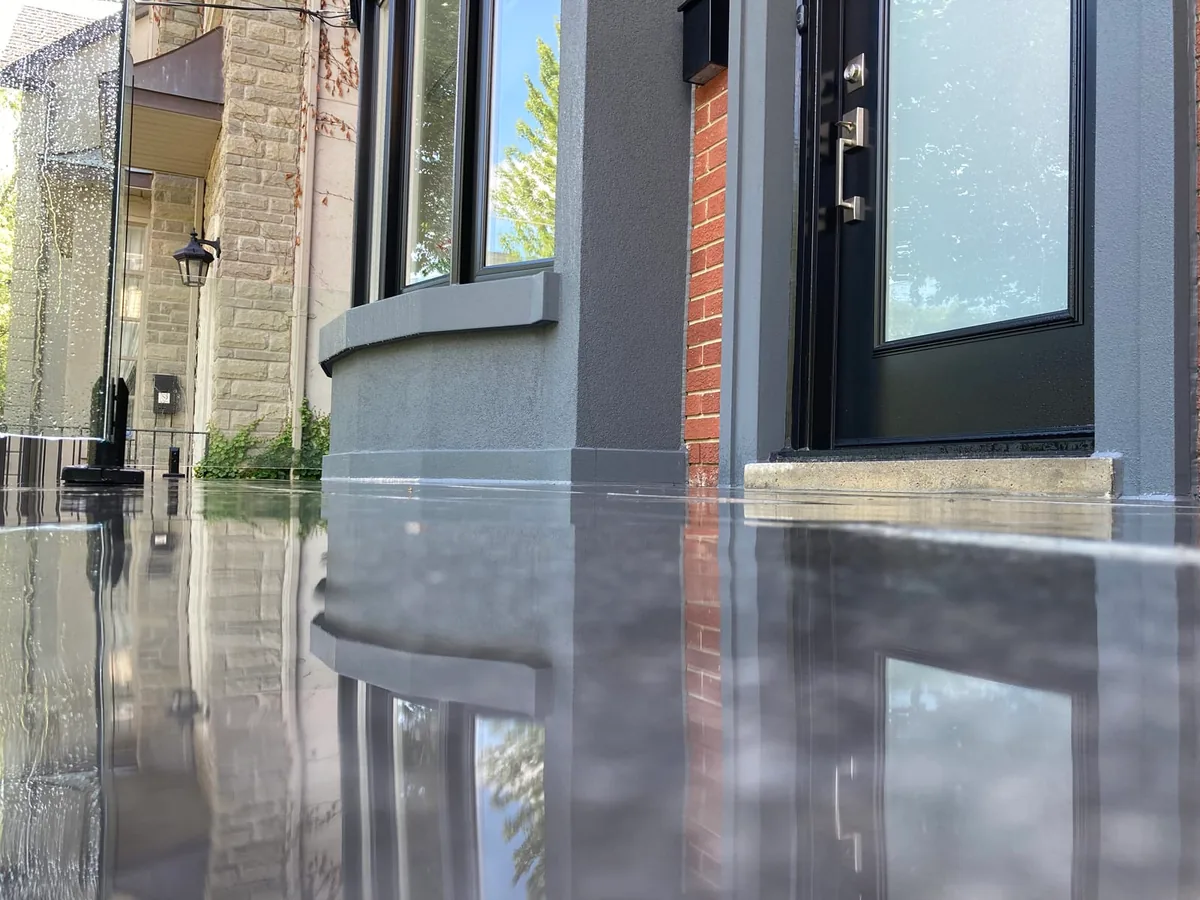 A low-angle view of the stone porch flooring near the black door, with brick accents reflected.