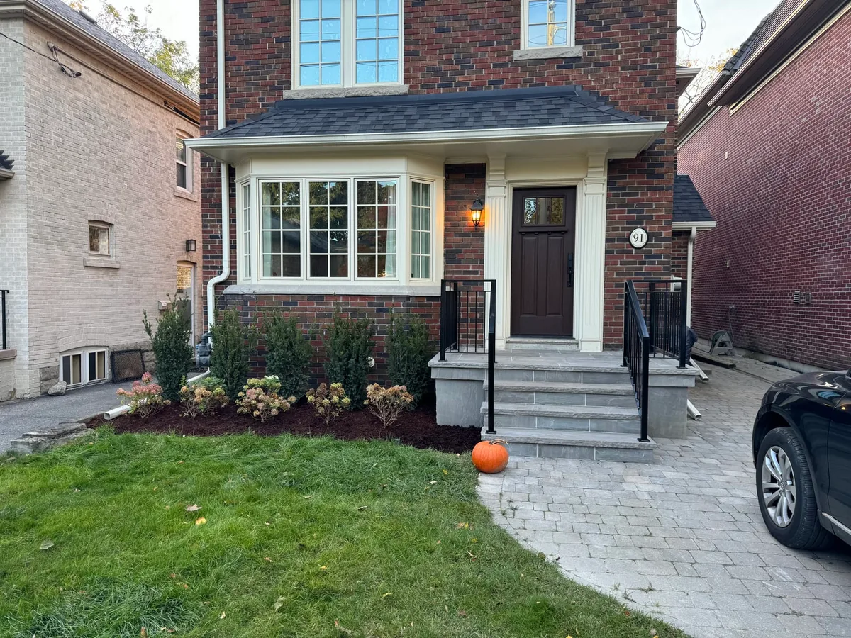 A brick house front with new stone steps, black railings, and an interlock driveway.