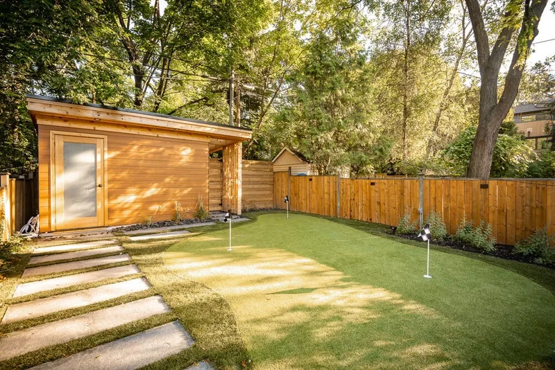A backyard with a wood shed, artificial turf lawn with small lighted markers, and a stepping-stone path.