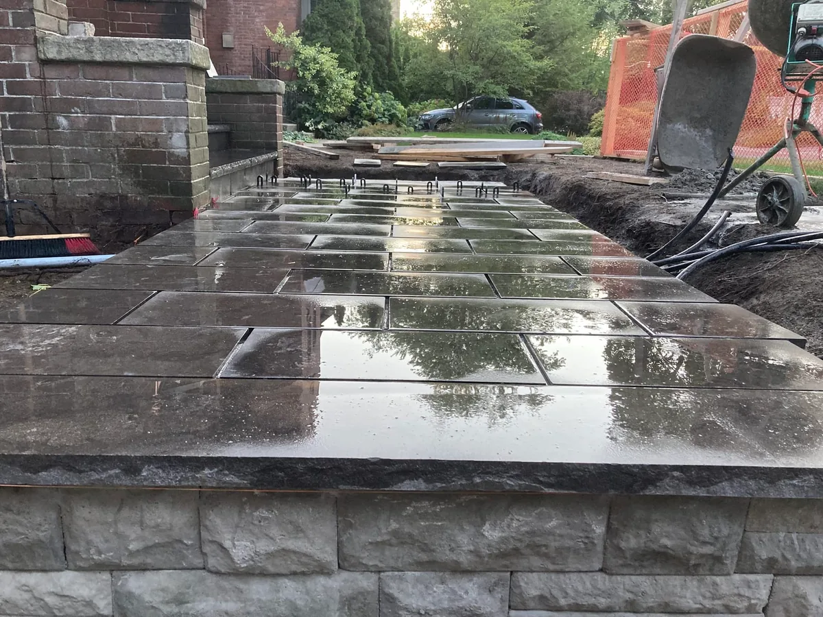 A wider view of the stone-clad wall coping with a cement mixer and safety fencing.