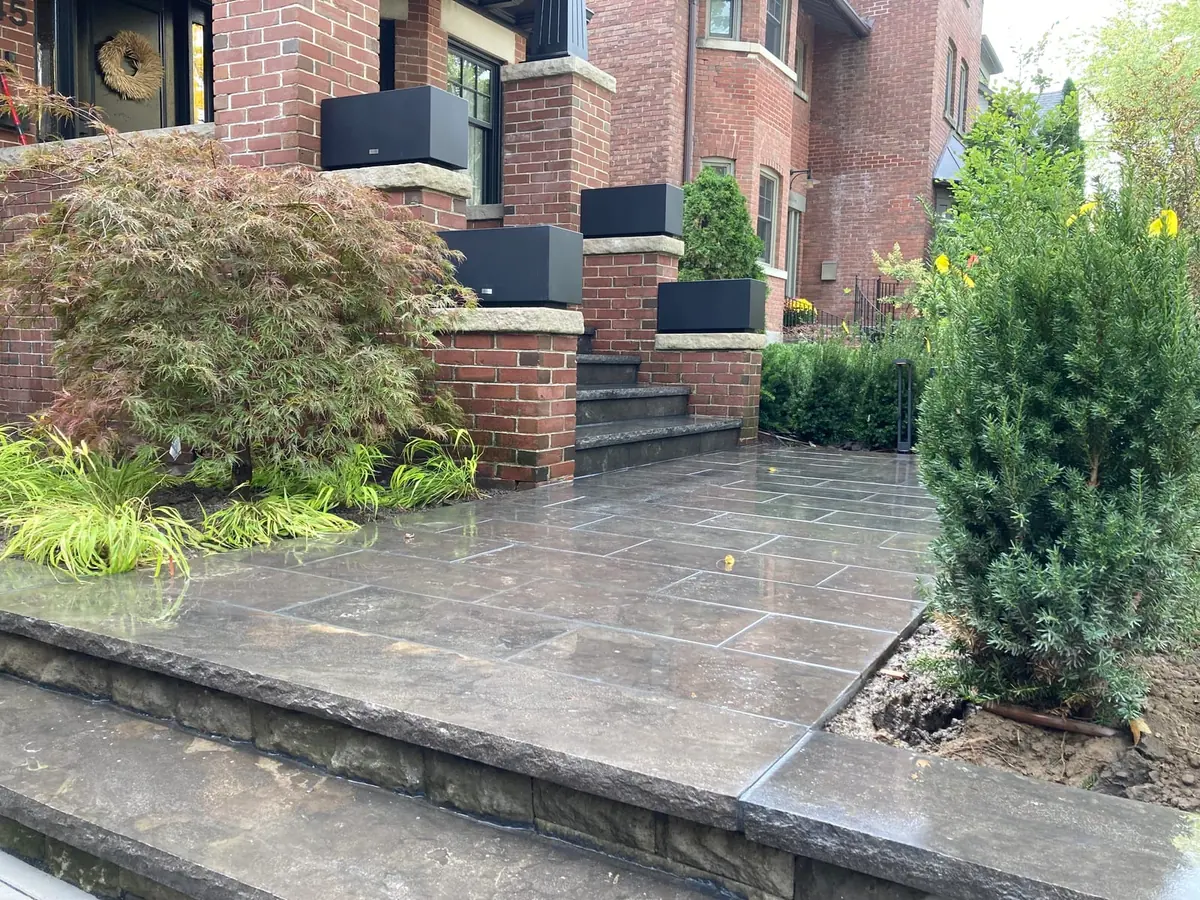 A finished concrete patio slab with a broom finish against a brick house, with a covered grill nearby.