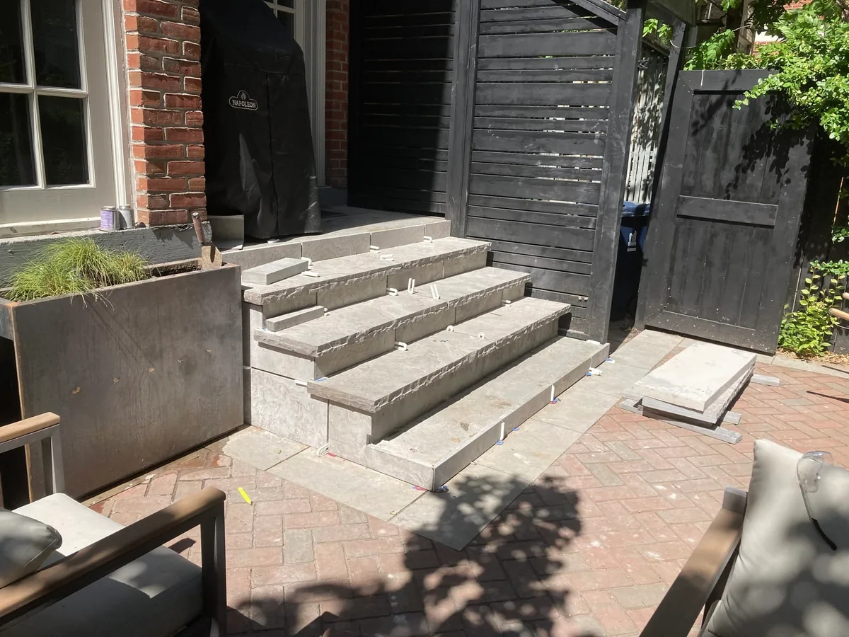 A closer view of the steps with a planter and a garbage bin beside a dark slat fence.