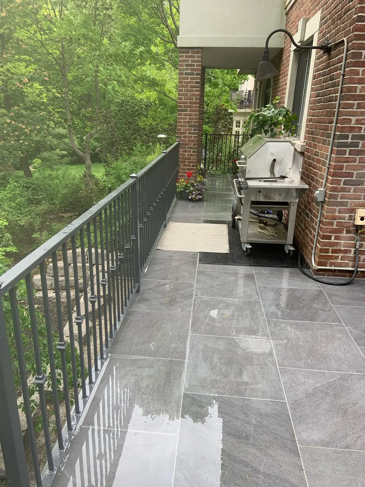 The balcony patio with a grill and a planter near a brick wall.