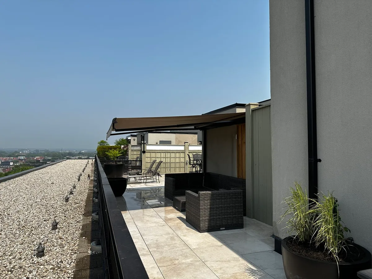 A rooftop terrace with a gravel section along the edge, wicker lounge furniture, and a retractable awning.