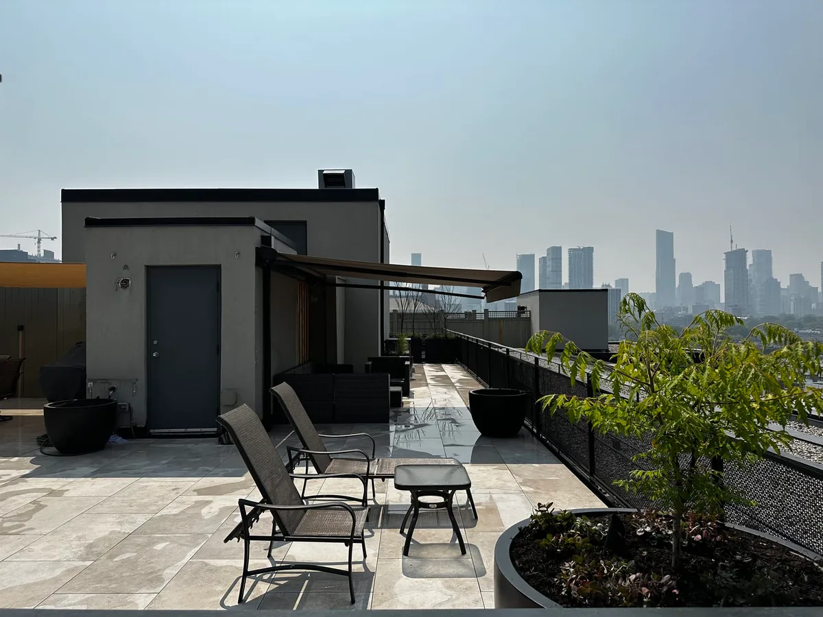 A rooftop patio seating area with two chairs and a small table beside a low building with an extended awning.