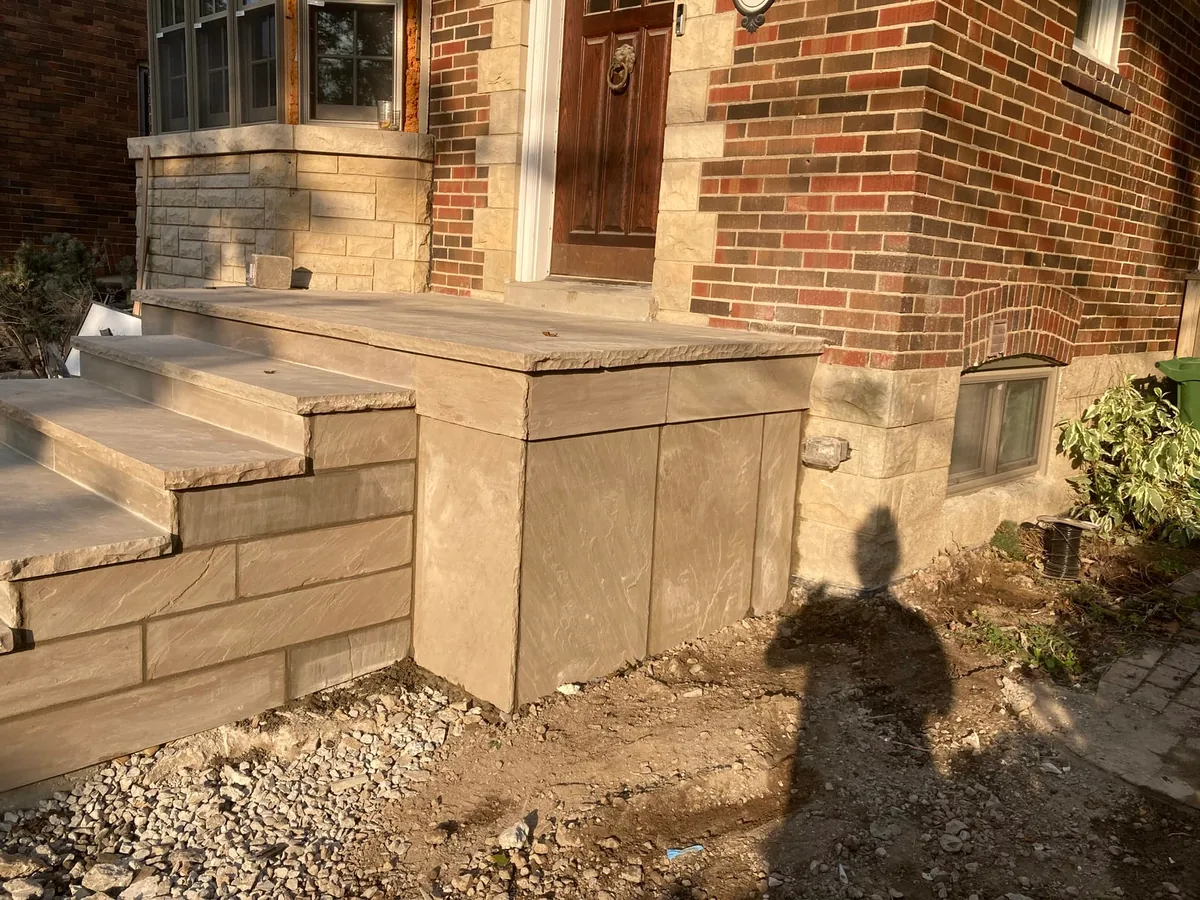 Front porch steps wrapped in tan stone cladding, with a shadow cast across the surface.