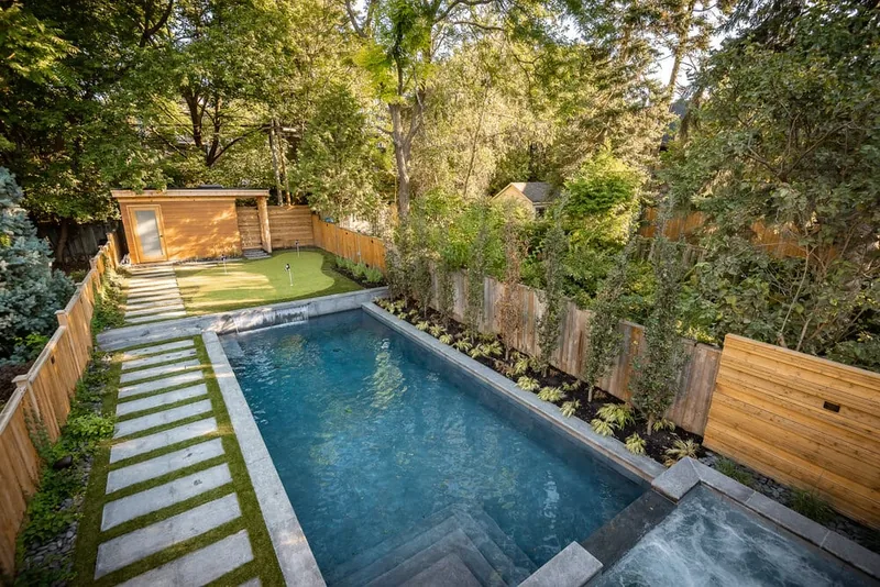 An elevated view of the backyard pool with stone coping, a wood shed, stepping pavers, and a spa in the corner.