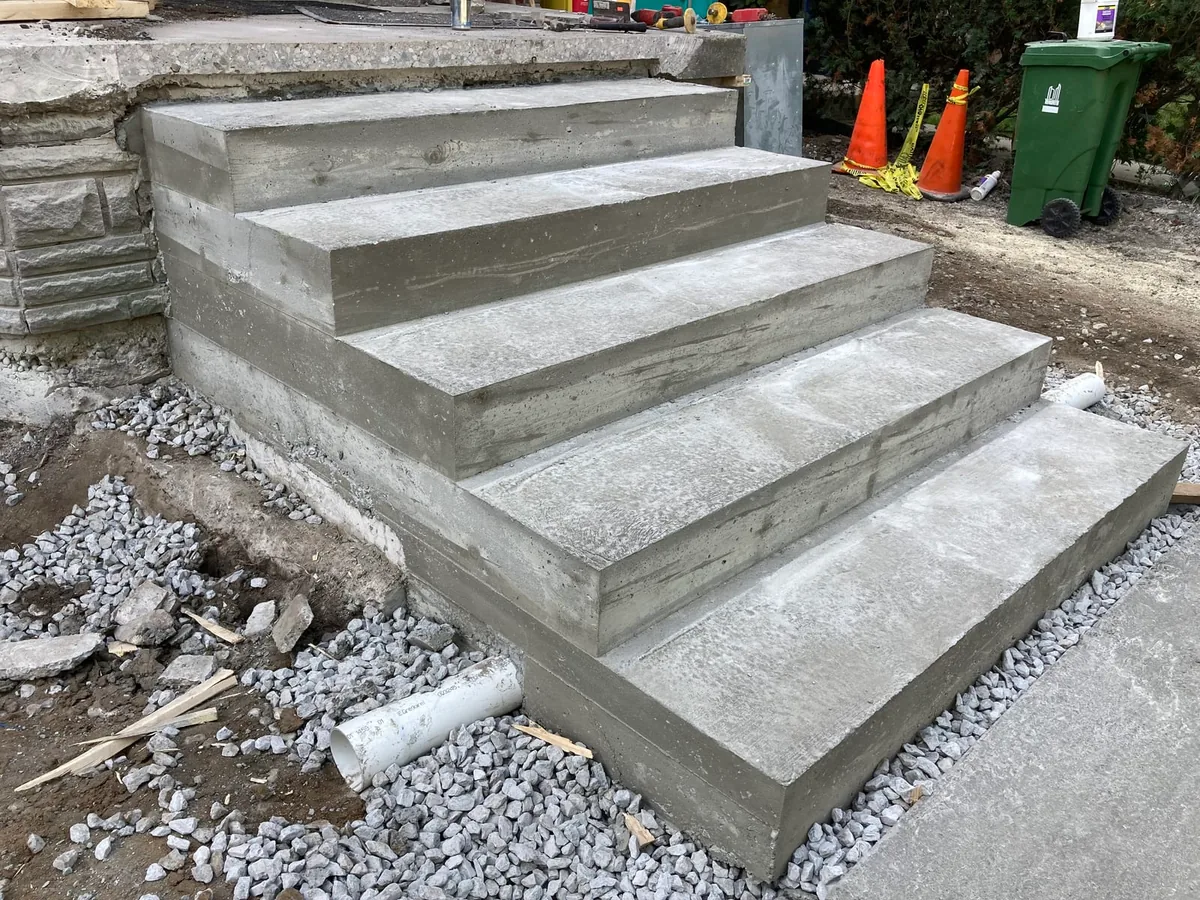 The finished poured concrete steps close up, with work gloves and traffic cones nearby.